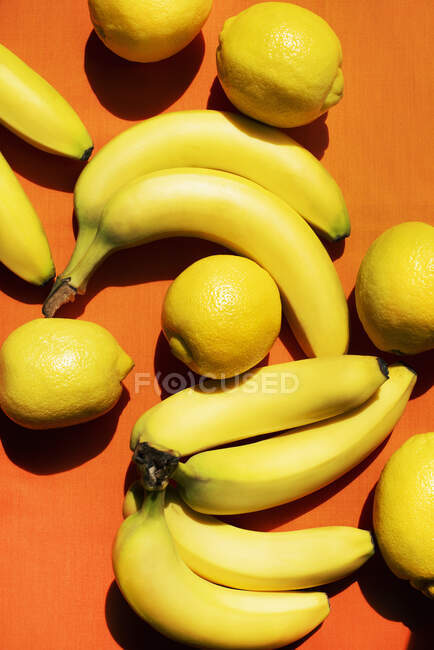 Vista aérea de bananas e limões sobre fundo laranja — Fotografia de Stock