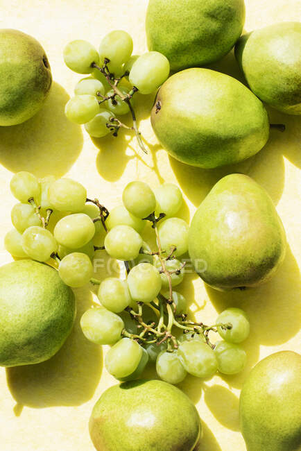 Blick von oben auf Birnen und Trauben auf gelbem Tischtuch — Stockfoto