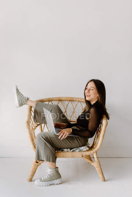 Mujer joven sentada en silla con portátil - foto de stock