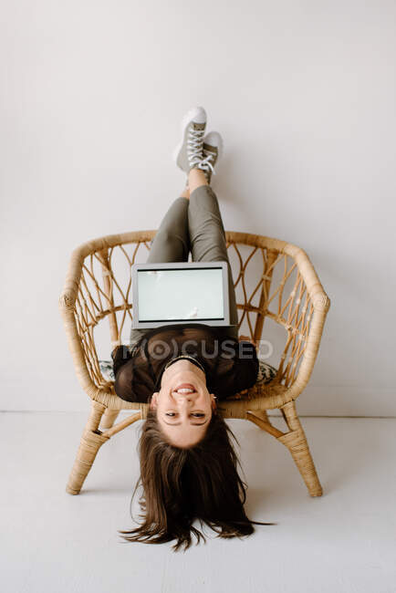 Mulher sentada de cabeça para baixo na cadeira com laptop — Fotografia de Stock