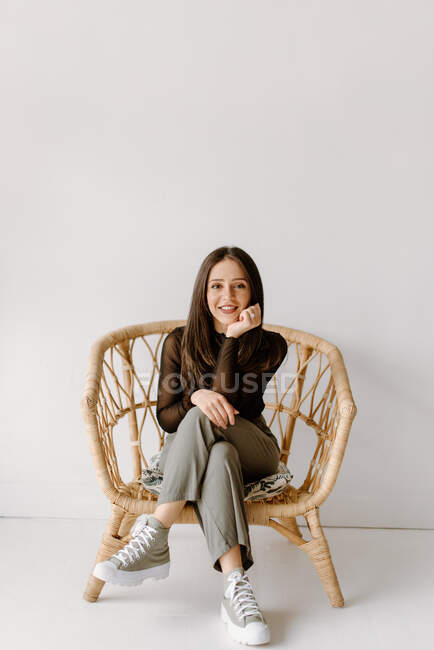Студійний знімок молодої жінки, що сидить у плетеному кріслі — стокове фото