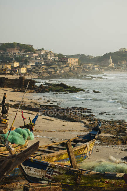 Ghana, Cape Coast, Vecchie barche da pesca sulla spiaggia con città in lontananza — Foto stock