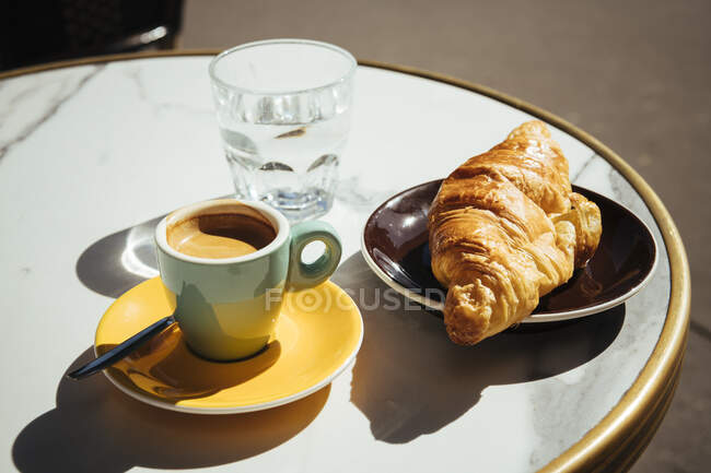 Francia, París, Croissant, café y vaso de agua en la mesa de café de la acera - foto de stock