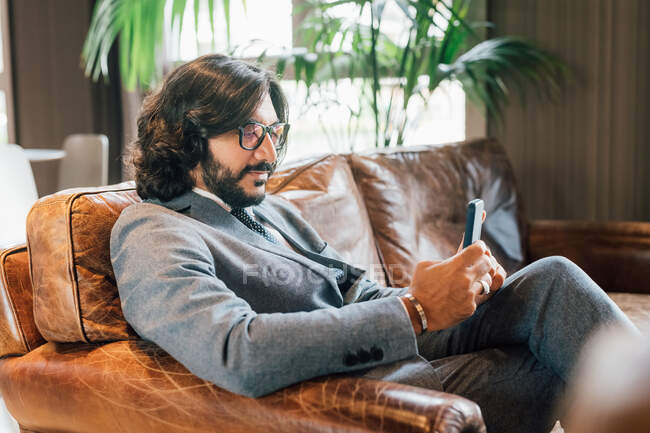 Italie, Homme d'affaires avec téléphone intelligent assis sur le canapé dans un studio créatif — Photo de stock