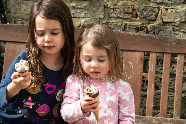 Regno Unito, Due ragazze (2-3, 4-5) con coni gelato sulla panchina — Foto stock