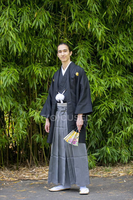 UK, Portrait of young man wearing kimono holding fan in park — Stock Photo