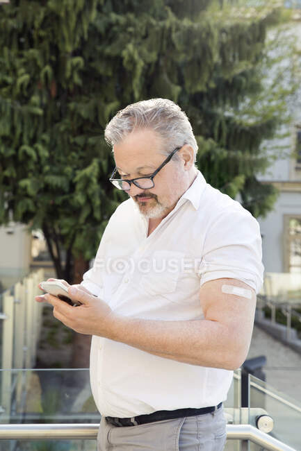 Austria, Vienna, Man with adhesive bandage on arm using smart phone outdoors — Stock Photo