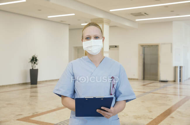 Austria, Vienna, Portrait of nurse in face mask holding clipboard in hospital — Stock Photo