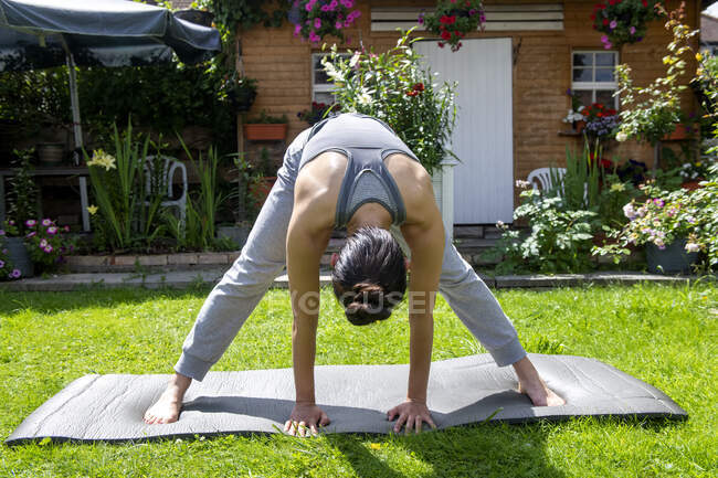 Reino Unido, Londres, Mujer haciendo yoga en el césped delante de la casa - foto de stock