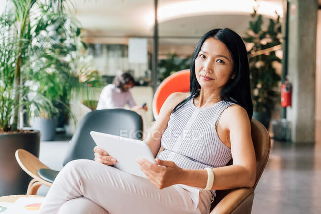 Italy, Woman sitting in armchair with digital tablet in creative studio — Stock Photo