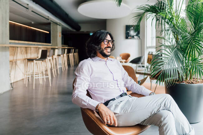 Italia, Hombre sonriente sentado en un sillón en un estudio creativo - foto de stock