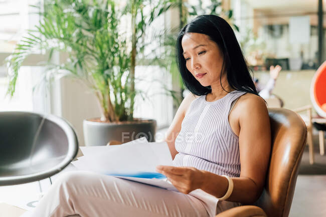 Italy, Woman sitting in armchair and reading documents in creative studio — Stock Photo