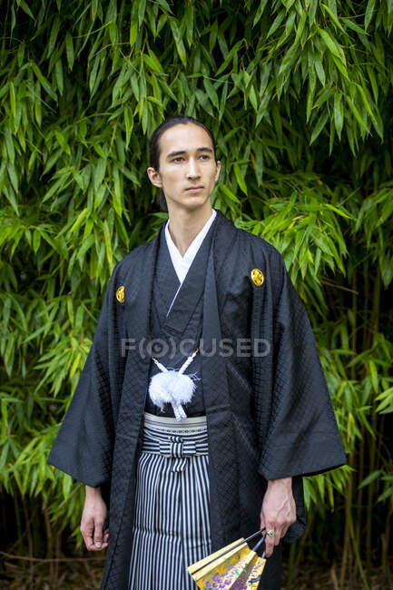 UK, Portrait of young man wearing kimono holding fan in park — Stock Photo