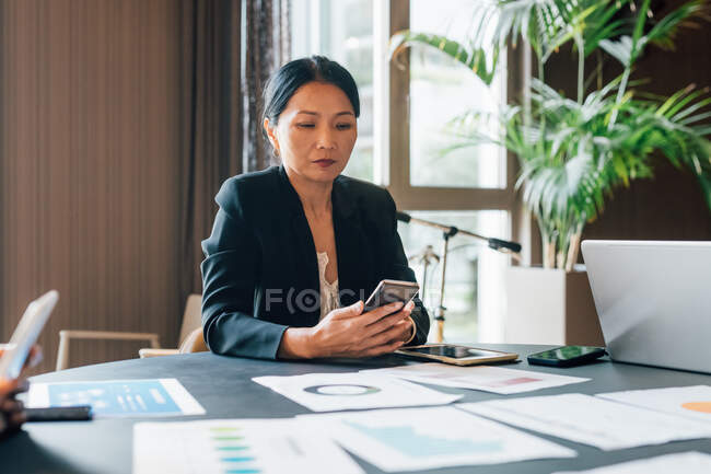 Italy, Businesswoman using smart phone at table in creative studio — Stock Photo