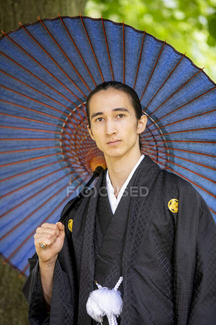Royaume-Uni, Portrait d'un jeune homme portant un kimono tenant un parasol dans un parc — Photo de stock