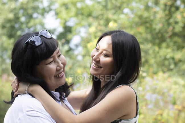 Alemania, Friburgo, Madre sonriente e hija adulta abrazándose al aire libre - foto de stock