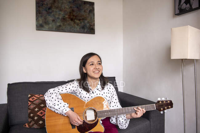 Mulher sorridente tocando guitarra acústica na sala de estar — Fotografia de Stock