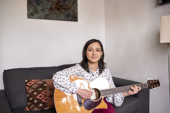 Улыбающаяся женщина играет на акустической гитаре в гостиной — стоковое фото
