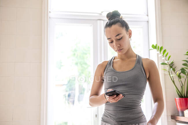 UK, London, Woman in tank top looking at smart phone at home — Stock Photo