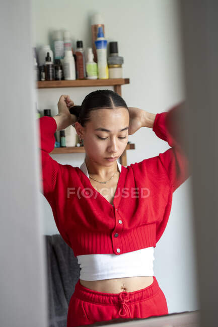 Великобритания, Лондон, Женщина в красной одежде, делающая волосы перед зеркалом — стоковое фото