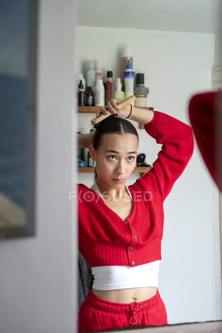 UK, London, Woman in red clothingdoing hair in front of mirror — Stock Photo