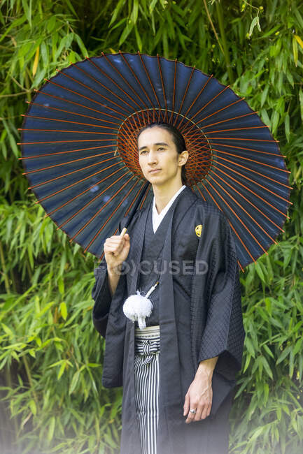 UK, Portrait of young man wearing kimono holding parasol in park — Stock Photo