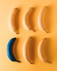 Банани на жовтому тлі, один кольоровий з синьою фарбою — стокове фото