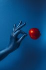 Main dans la peinture bleue tenant pomme rouge sur fond bleu — Photo de stock