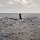 Retrato traseiro de mulher de vestido preto em pé na superfície da água no mar — Fotografia de Stock