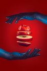 Нарізане яблуко між двома руками на червоному тлі — стокове фото