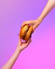 Cropped image of female hands holding burger against purple background — Stock Photo