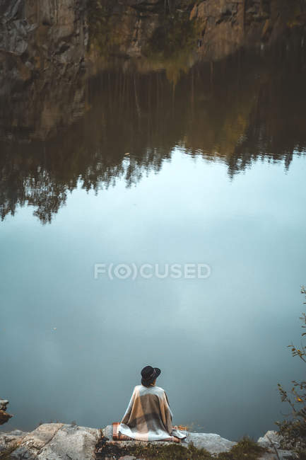 Femme assise sur des rochers près du lac — Photo de stock