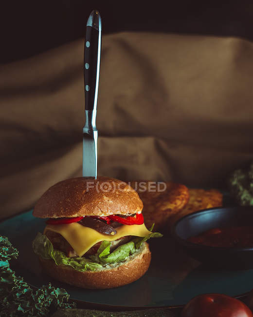Knife in burger with bread and vegetables — Stock Photo