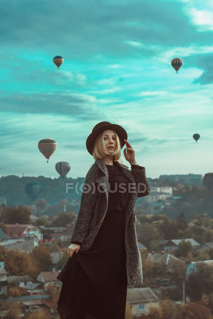 Porträt einer blonden Frau mit Hut und Luftballons über der Stadt — Stockfoto