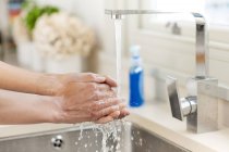 Close-up of woman washing hands under tap in kitchen. — Stock Photo