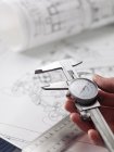 Engineer holding dial calipers over blueprints on table. — Stock Photo