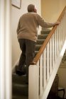 Rear view of senior man climbing up at home stairs. — Stock Photo