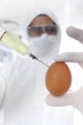 Wissenschaftler injiziert Ei mit Spritze mit weißer Flüssigkeit, konzeptionelles Bild. — Stockfoto
