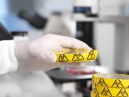Scientifique tenant une boîte de Pétri avec avertissement de danger biologique dans un laboratoire de microbiologie . — Photo de stock