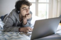 Junger Mann mit Kopfhörer benutzt Laptop im Schlafzimmer. — Stockfoto