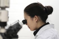 Жіночий технік у білому пальто з використанням мікроскопа . — стокове фото