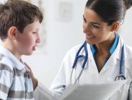 Pediatra hablando con un niño de edad elemental . - foto de stock