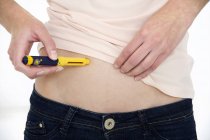 Cropped view of woman making injection into stomach with medical device. — Stock Photo