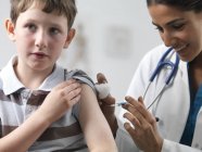 Female pediatrician giving injection to elementary age boy. — Stock Photo