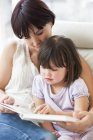 Mother and daughter reading on sofa. — Stock Photo