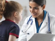 Pediatra hablando con niña en edad preescolar . - foto de stock