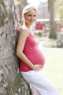 Glückliche schwangere Frau lehnt sich an Baum — Stockfoto