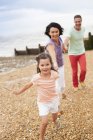 Genitori che corrono sulla spiaggia mano nella mano con la figlia . — Foto stock