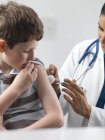 Pediatra do sexo feminino que dá injeção ao menino de idade elementar . — Fotografia de Stock