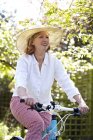 Mature woman in sunhat cycling in garden. — Stock Photo